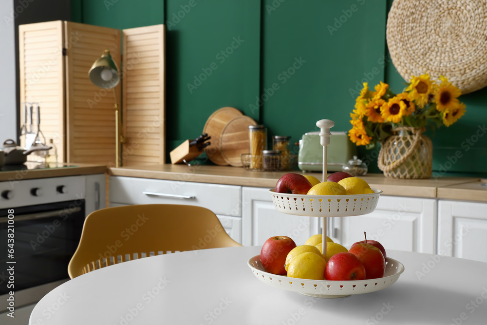 Stand with fresh fruits on white dining table in modern kitchen