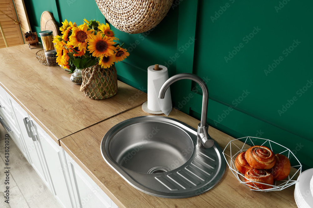 Wooden counters with sink, cinnamon rolls and sunflowers in modern kitchen