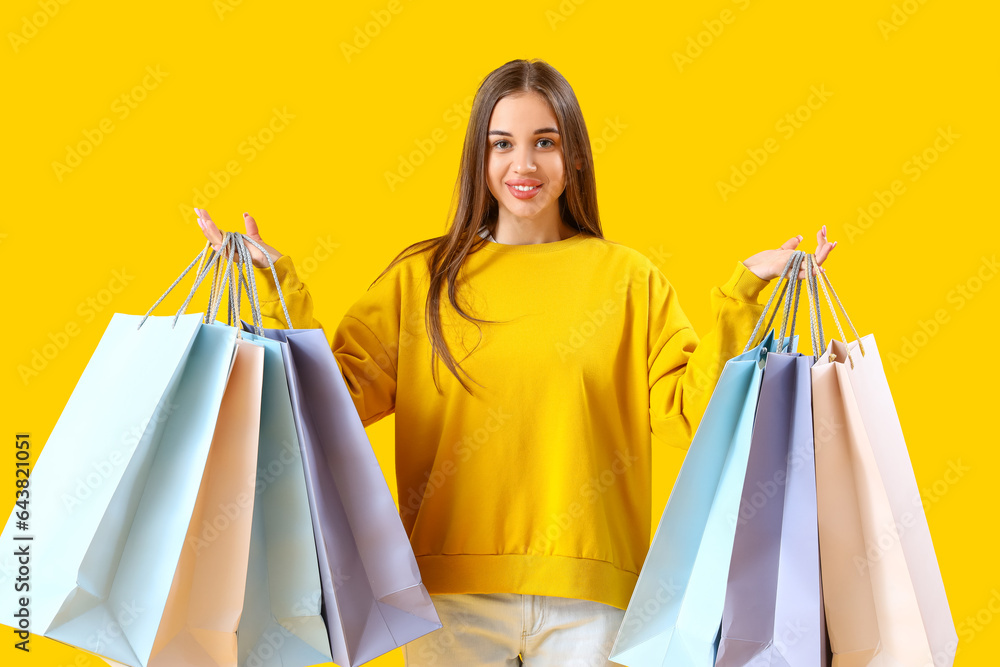 Young woman with shopping bags on yellow background