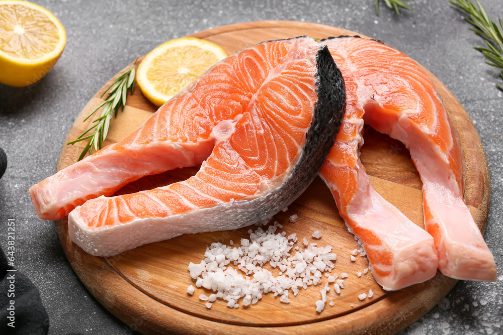 Wooden board with raw salmon steaks and different spices on grey background