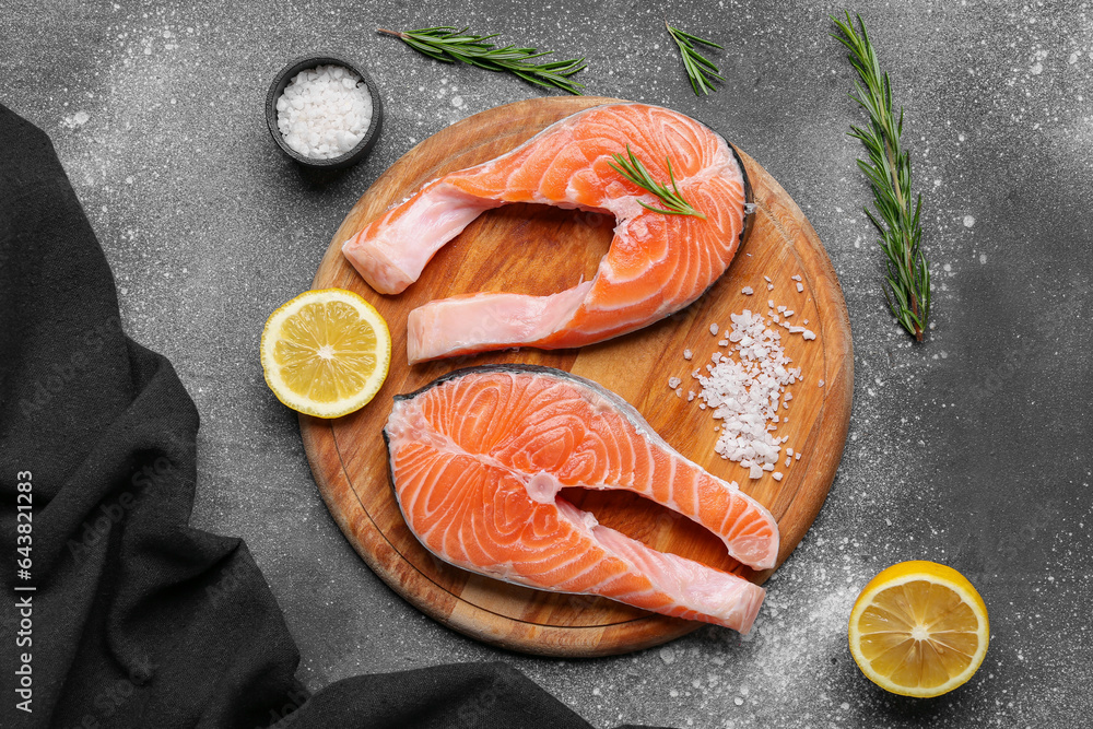 Wooden board with raw salmon steaks and different spices on grey background