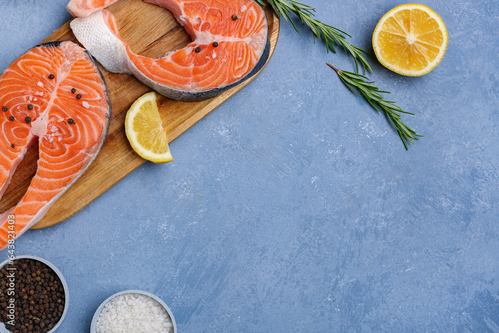 Wooden board with raw salmon steaks and different spices on blue background