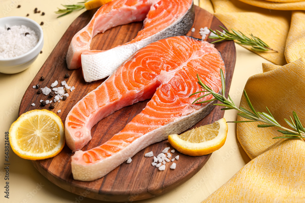 Wooden board with raw salmon steaks and different spices on yellow background