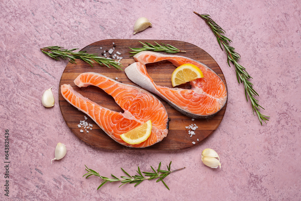 Wooden board with raw salmon steaks and different spices on pink background