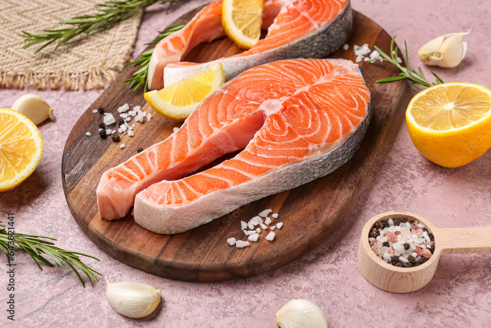 Wooden board with raw salmon steaks and different spices on pink background