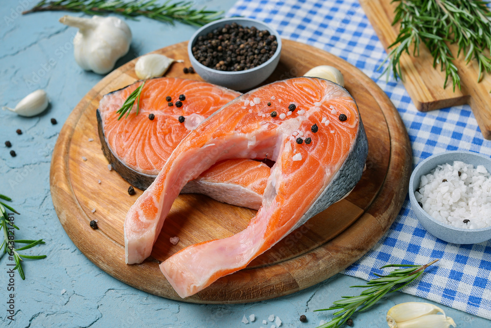 Wooden board with raw salmon steaks and different spices on blue background