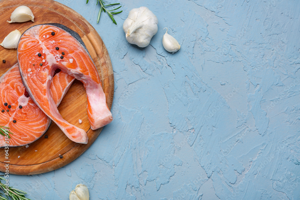 Wooden board with raw salmon steaks and different spices on blue background