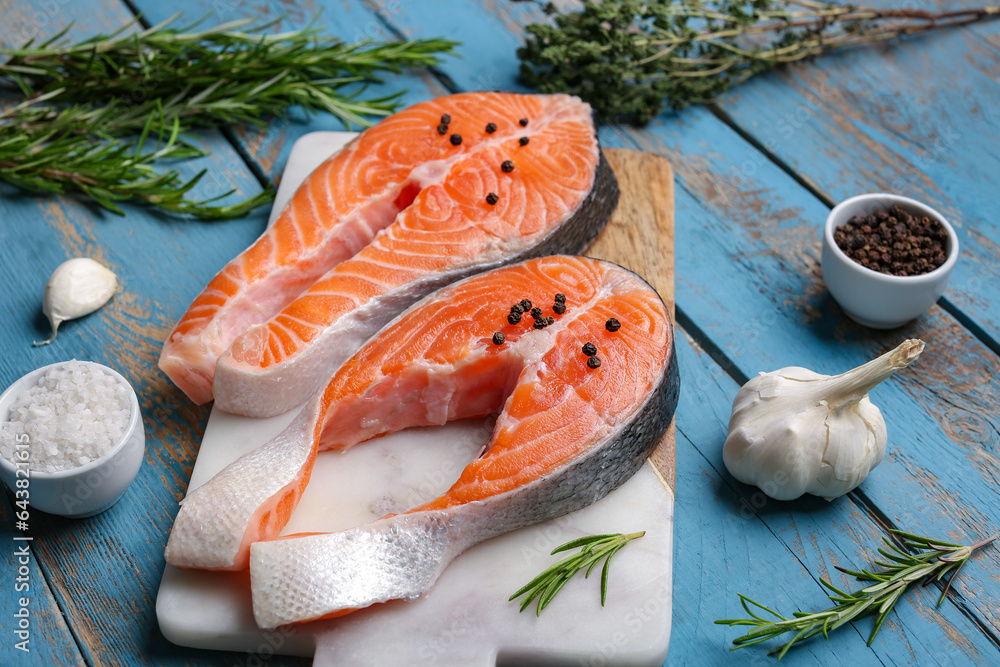 Board with raw salmon steaks and different spices on blue wooden background