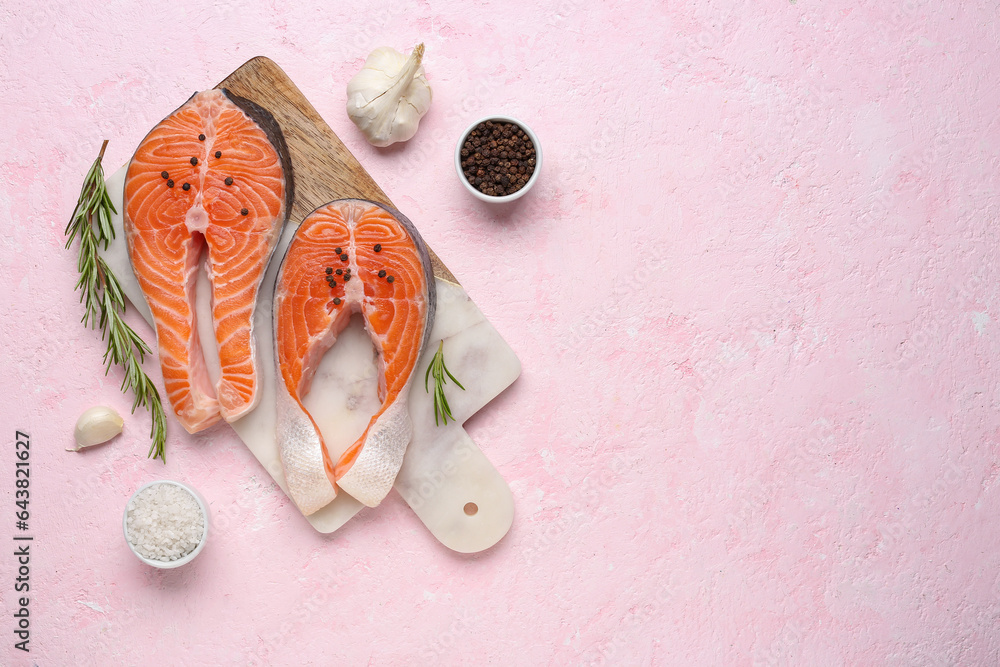 Board with raw salmon steaks and different spices on pink background