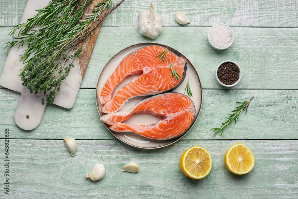 Plate with raw salmon steaks and different spices on green wooden background