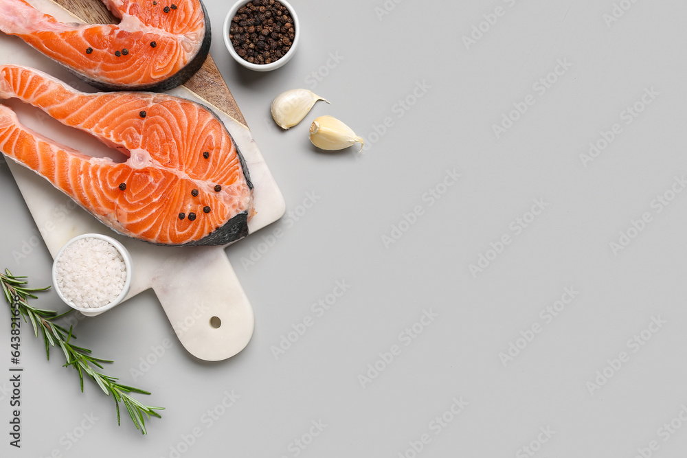 Board with raw salmon steaks and different spices on grey background