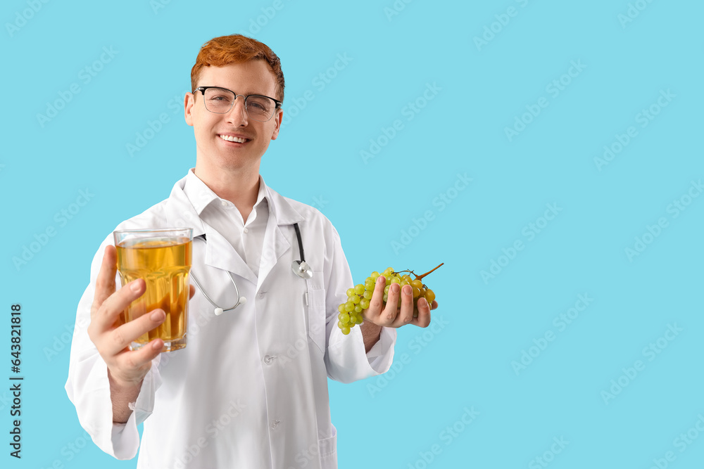 Male doctor with glass of juice and grape on blue background