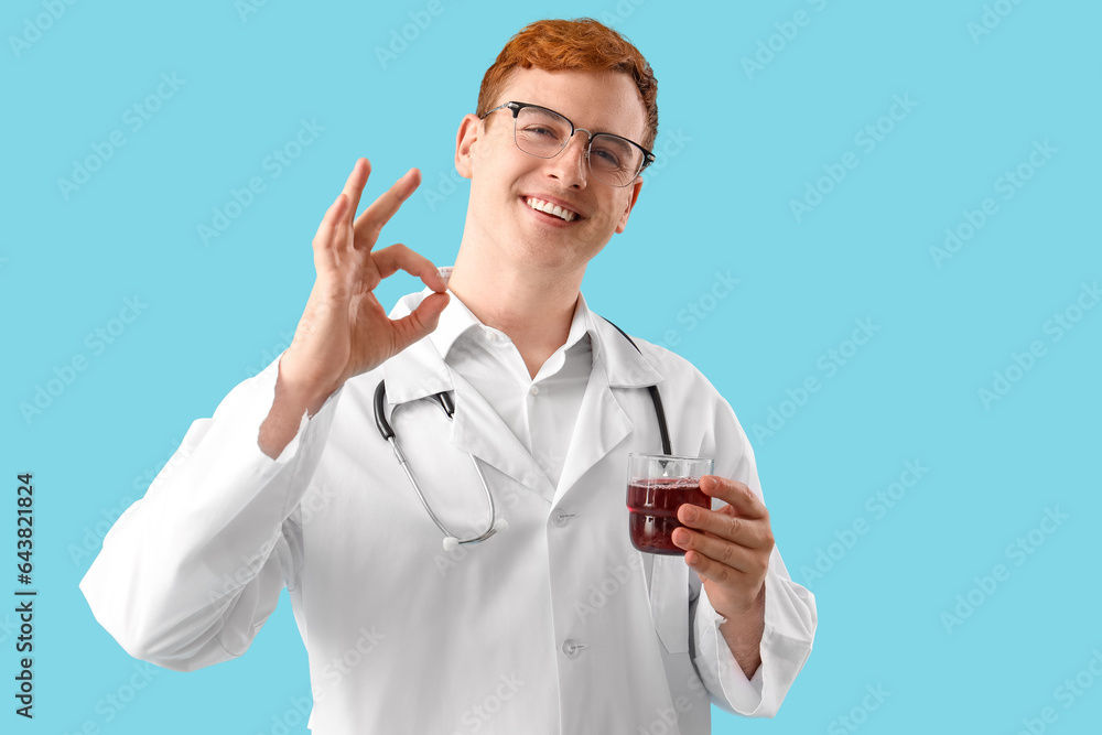 Male doctor with glass of juice showing OK on blue background