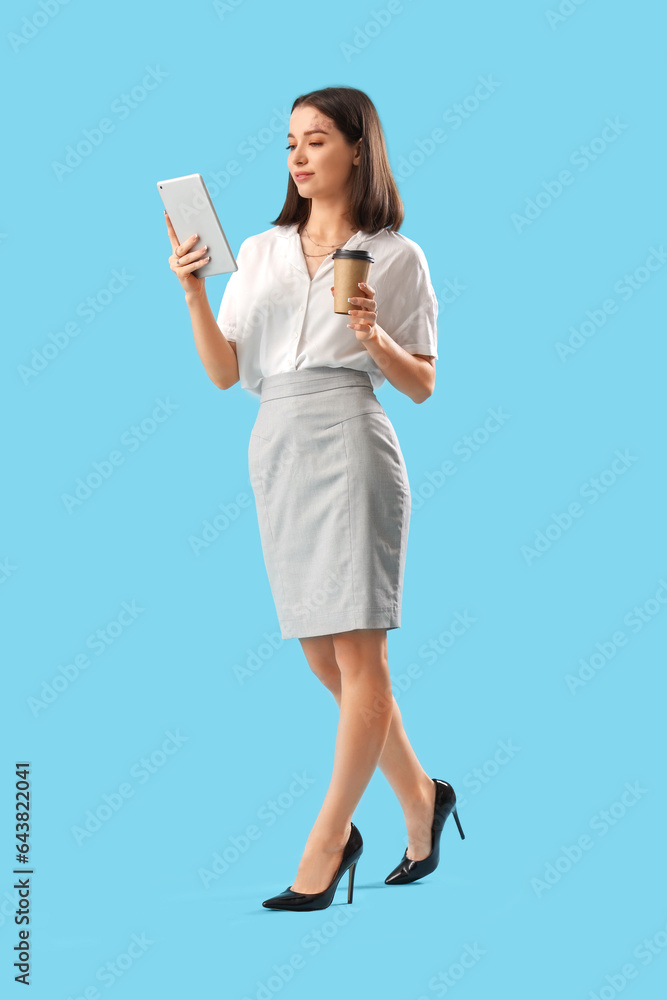 Young businesswoman with tablet computer and cup of coffee on blue background