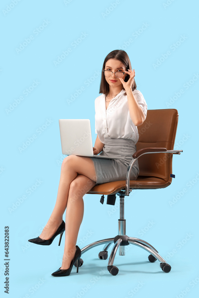 Young businesswoman with laptop sitting in chair on blue background