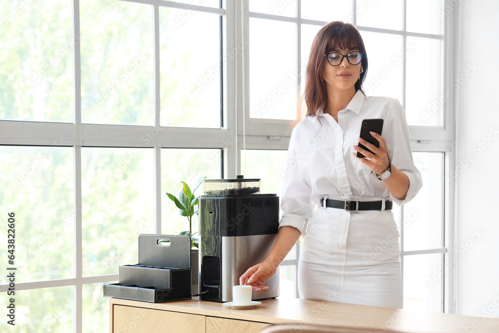 Beautiful businesswoman with mobile phone and cup of coffee in office