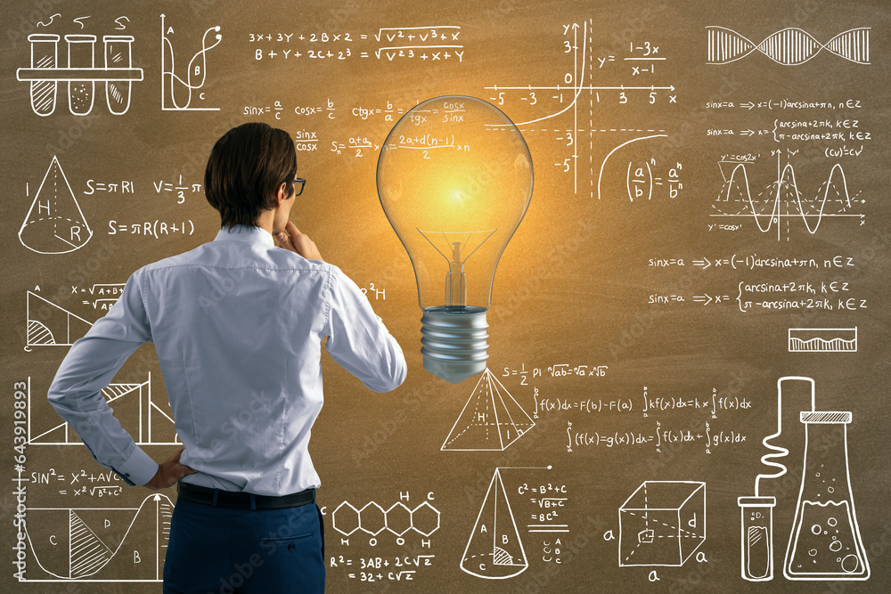 Back view of attractive thoughtful young european businessman with glowing light bulb on chalkboard 