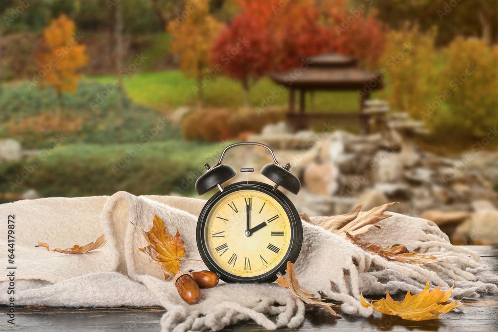 Alarm clock, plaid, acorns and autumn leaves on table outdoors