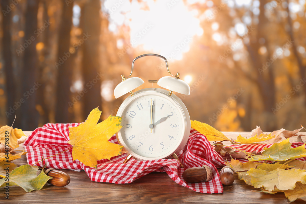 Alarm clock and autumn leaves on table outdoors. Daylight saving time end