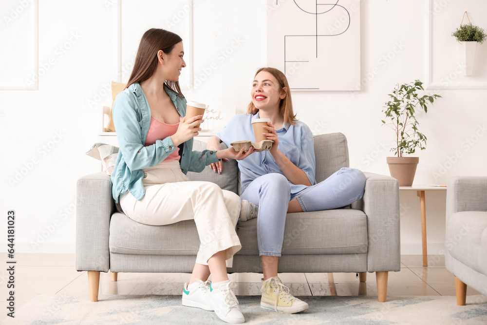 Female friends with cups of coffee sitting on sofa at home