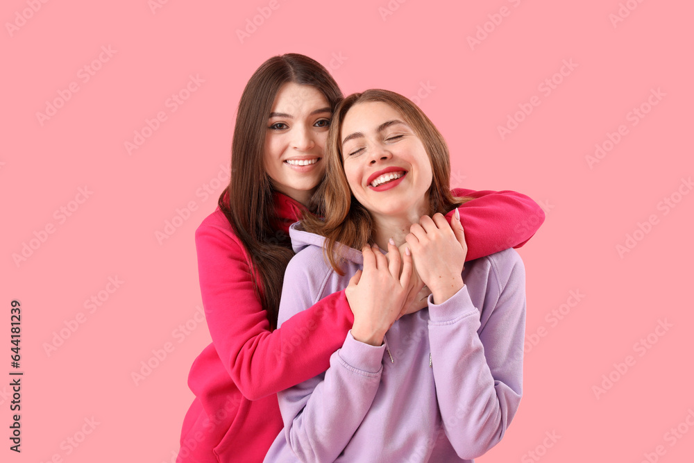 Female friends hugging on pink background