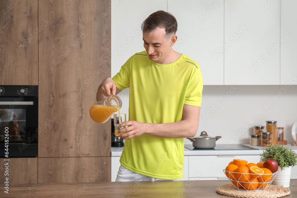 Young man pouring orange juice into glass in kitchen