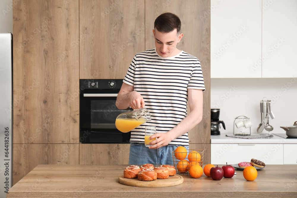 Young man pouring orange juice into glass in kitchen