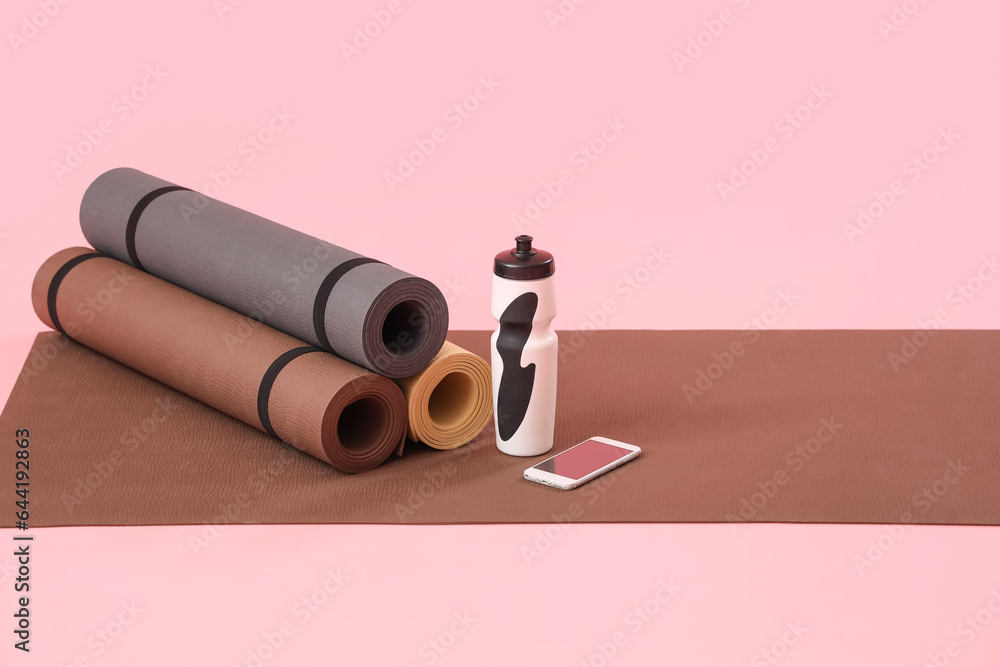 Fitness mats with bottle and mobile phone on pink background