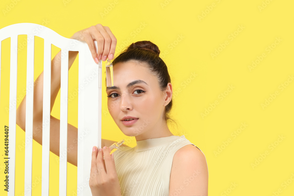 Beautiful young woman with ampules and folding screen on yellow background, closeup