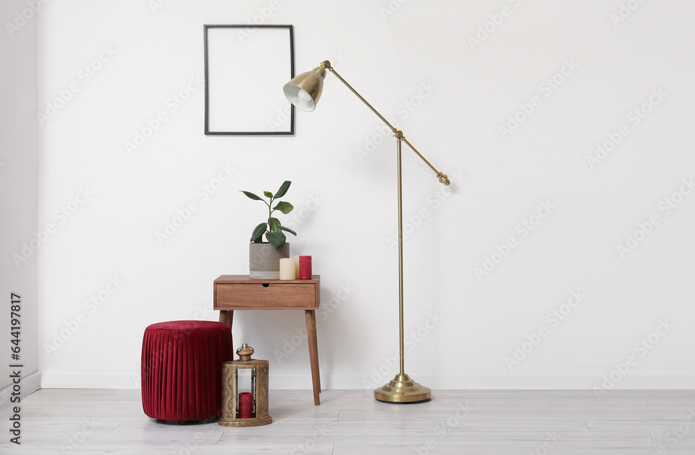 Interior of light room with plant on table, lamp and pouf