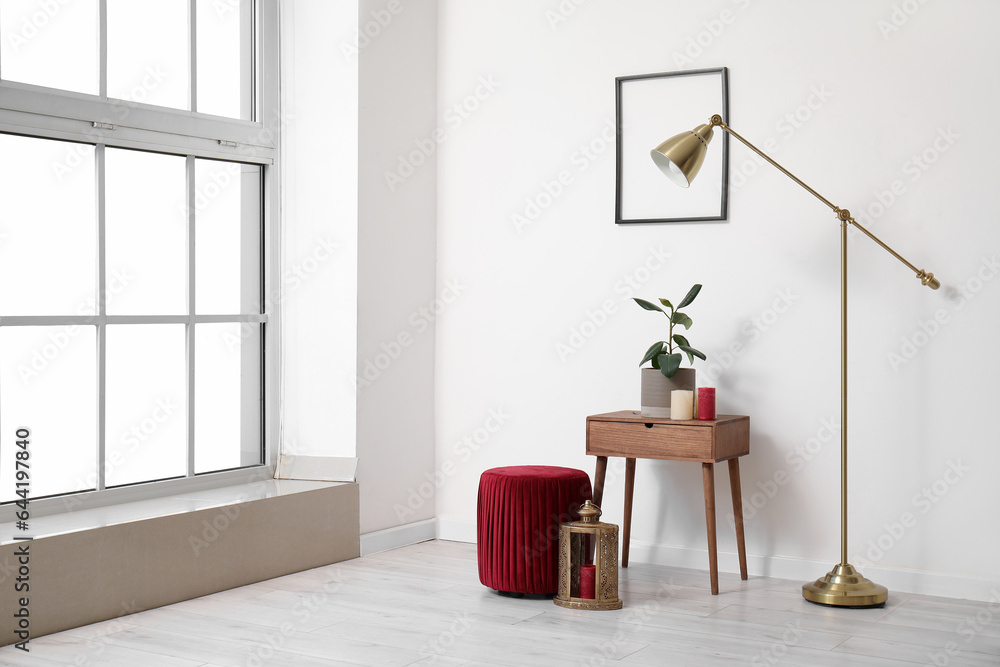 Interior of light room with plant on table, lamp and pouf