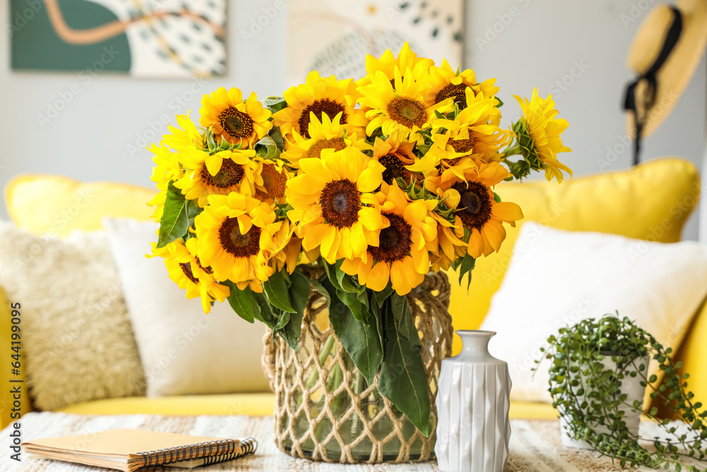 Vase with sunflowers, plant and notebook on table in living room