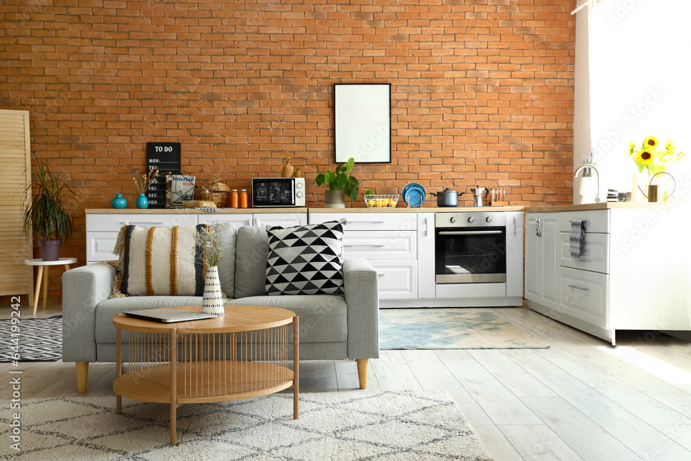 Interior of modern open space kitchen with grey sofa, coffee table and white counters