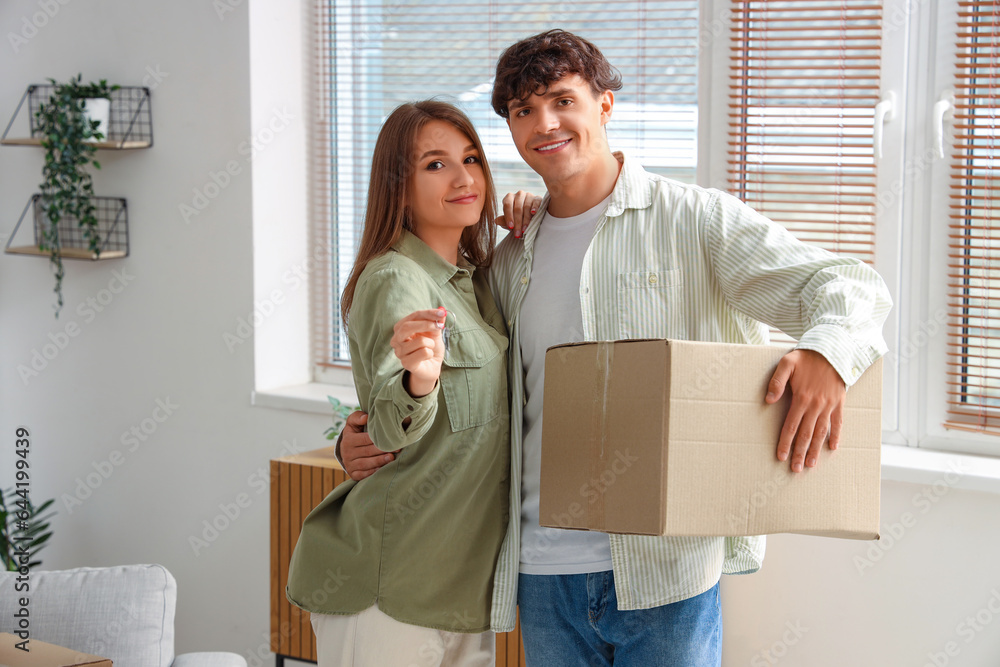 Young couple with keys and moving box in their new flat