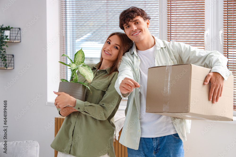 Young couple with keys and moving box in their new flat