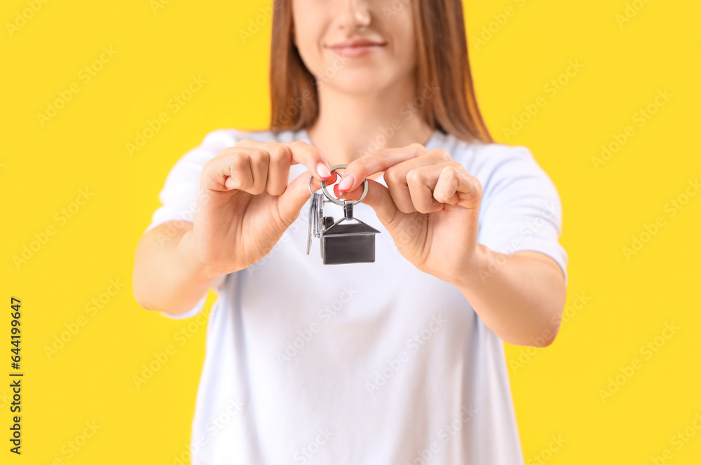 Young woman with keys from house on yellow background, closeup