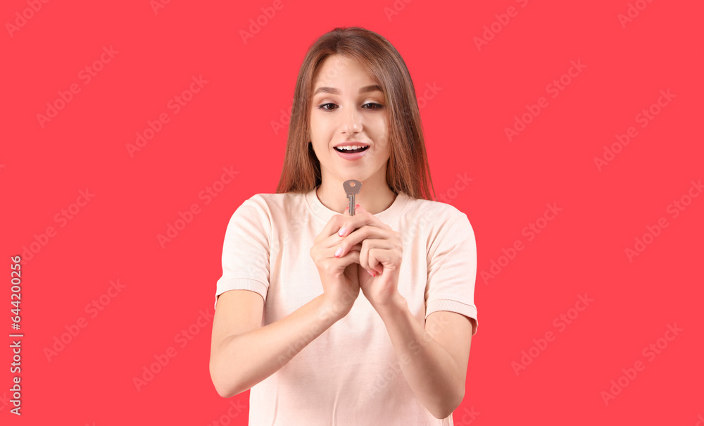 Young woman with key from house on red background