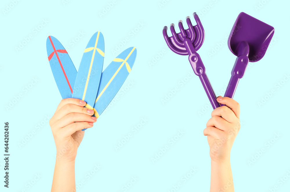 Female hands with mini surfboards and beach sand toys on blue background