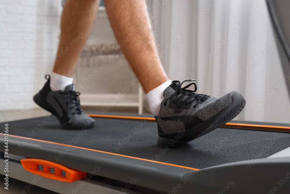 Sporty young man training on treadmill at home, closeup