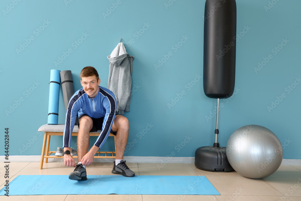 Sporty young man tying shoelaces before training in gym