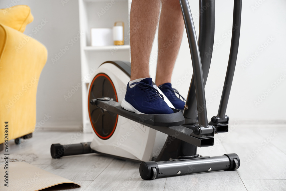 Sporty young man training on elliptical machine at home