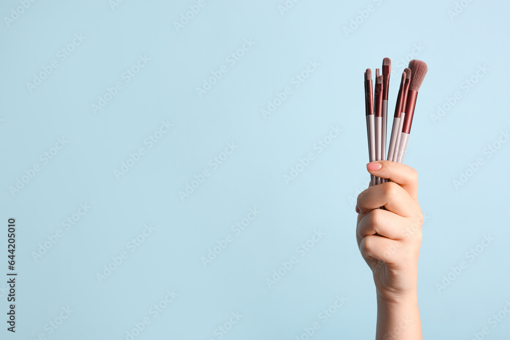 Female hand with makeup brushes on blue background