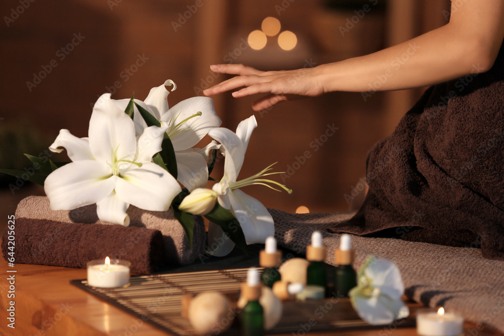 Young woman with lily flowers in dark spa salon, closeup