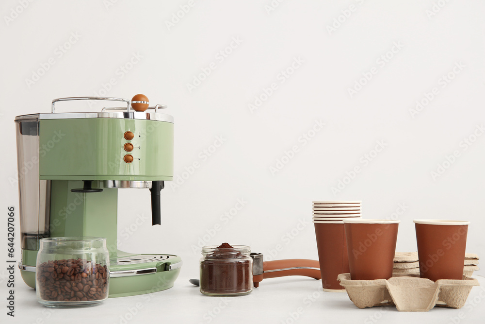 Modern coffee machine, takeaway cups, beans and powder on white background