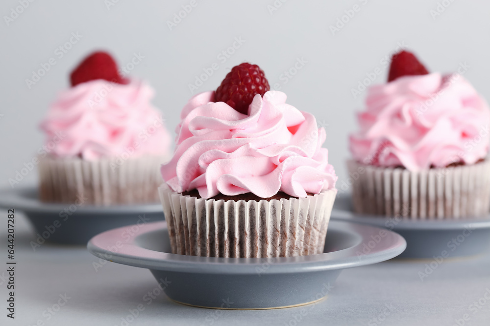 Plates with tasty raspberry cupcakes on grey background, closeup