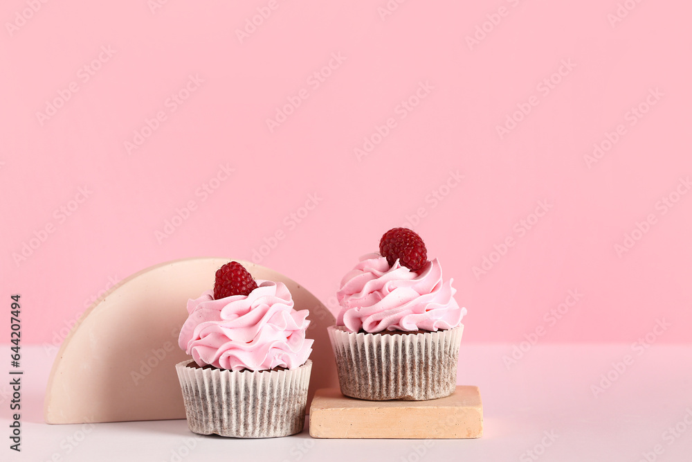 Decorative stand with tasty raspberry cupcakes on pink background