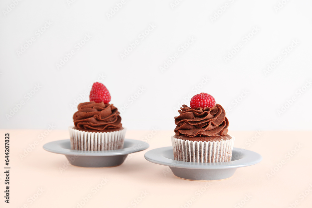 Plates of tasty chocolate cupcakes with raspberries on beige background