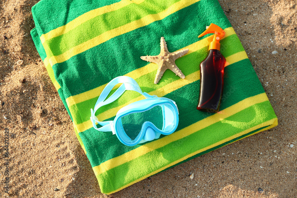 New swimming mask, sunscreen spray, starfish and towel on sand