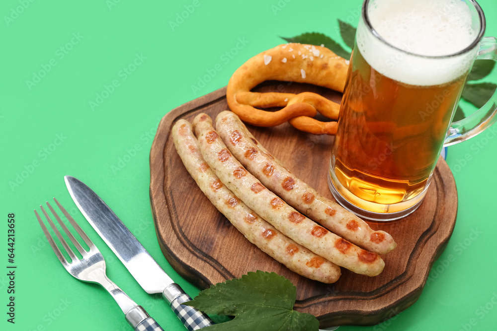 Wooden board with tasty Bavarian sausages, pretzel and mug of beer on green background. Oktoberfest 