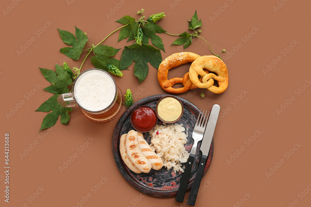 Plate with tasty Bavarian sausages, pretzels, sauerkraut, sauces and mug of beer on brown background